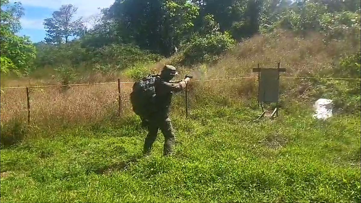 Tirador con uniforme de camuflaje y mochila disparando con pistola en el campo de tiro